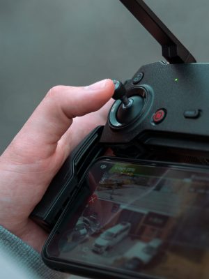 Close-up of a hand using a drone controller with live video feed on screen.